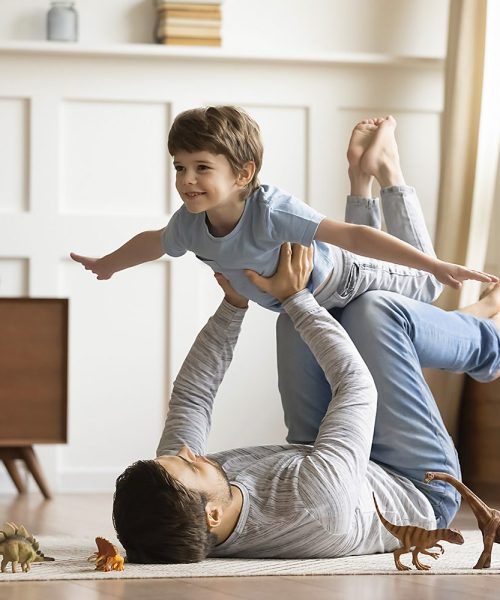 Joyful young man father lying on carpet floor, lifting excited happy little child son at home. Full length carefree two generations family having fun, practicing acroyoga in pair in living room.; Shutterstock ID 1646469193; Purchase Order: wsip